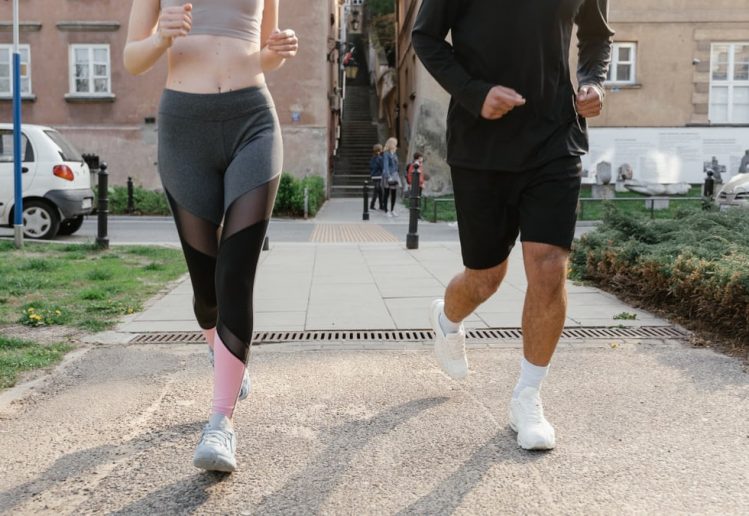 Fit couple jogging together on an urban sidewalk in sportswear.